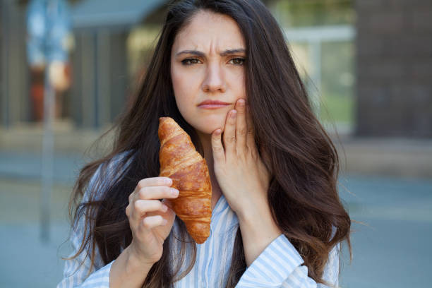 woman holding a croissant while frowning due to tooth pain