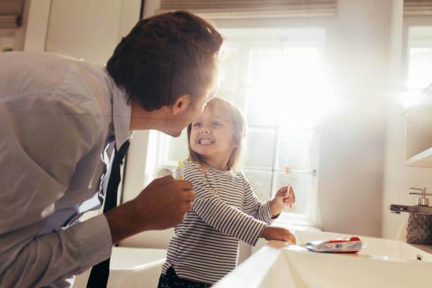 a child smiling at her dad while holding a toothbrush