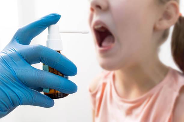 a hand holding a mouth spray in front of a kid with mouth wide open