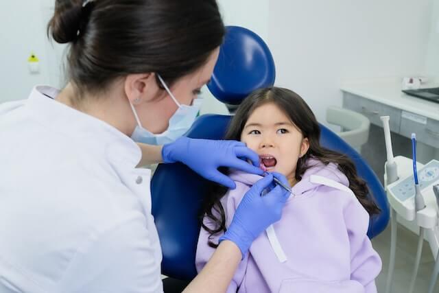 a dentist checking the little girl's teeth while sitting on the dentist chair