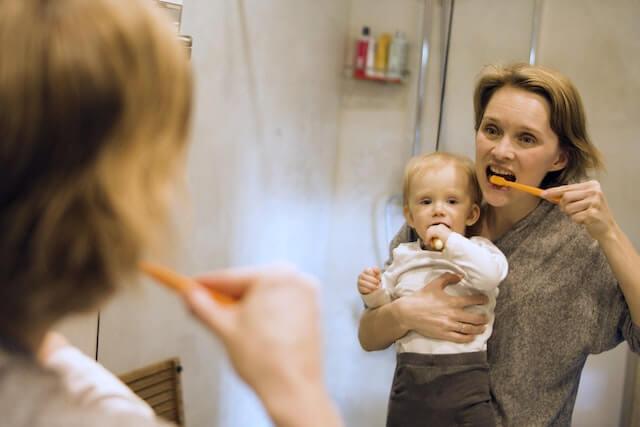 a mom and baby brushing their teeth in front of a mirror