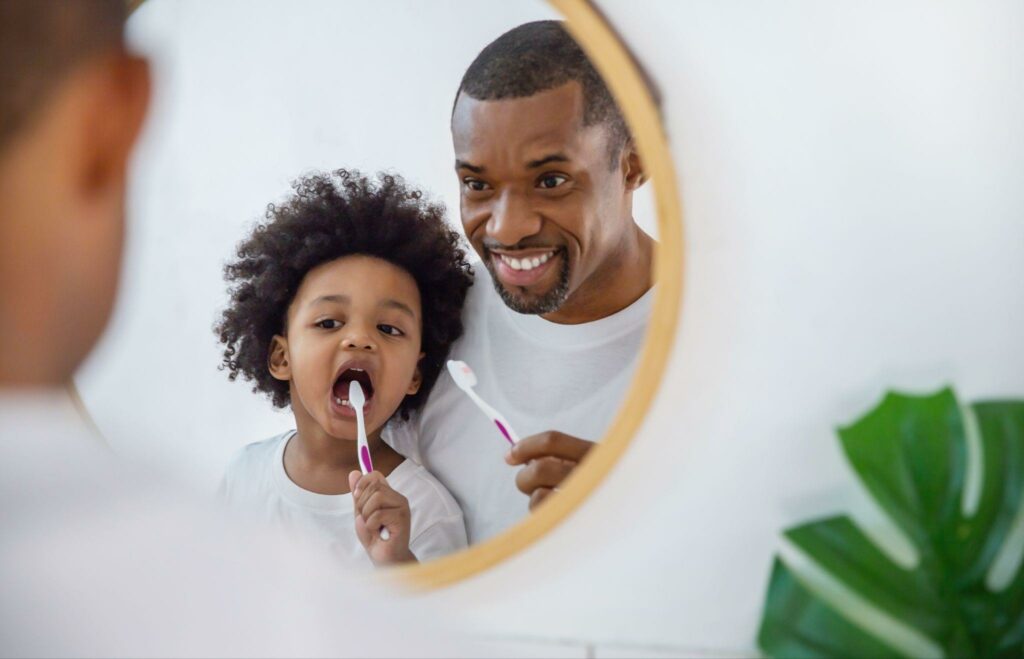 a father and daughter brushing their teeth in front of the mirror