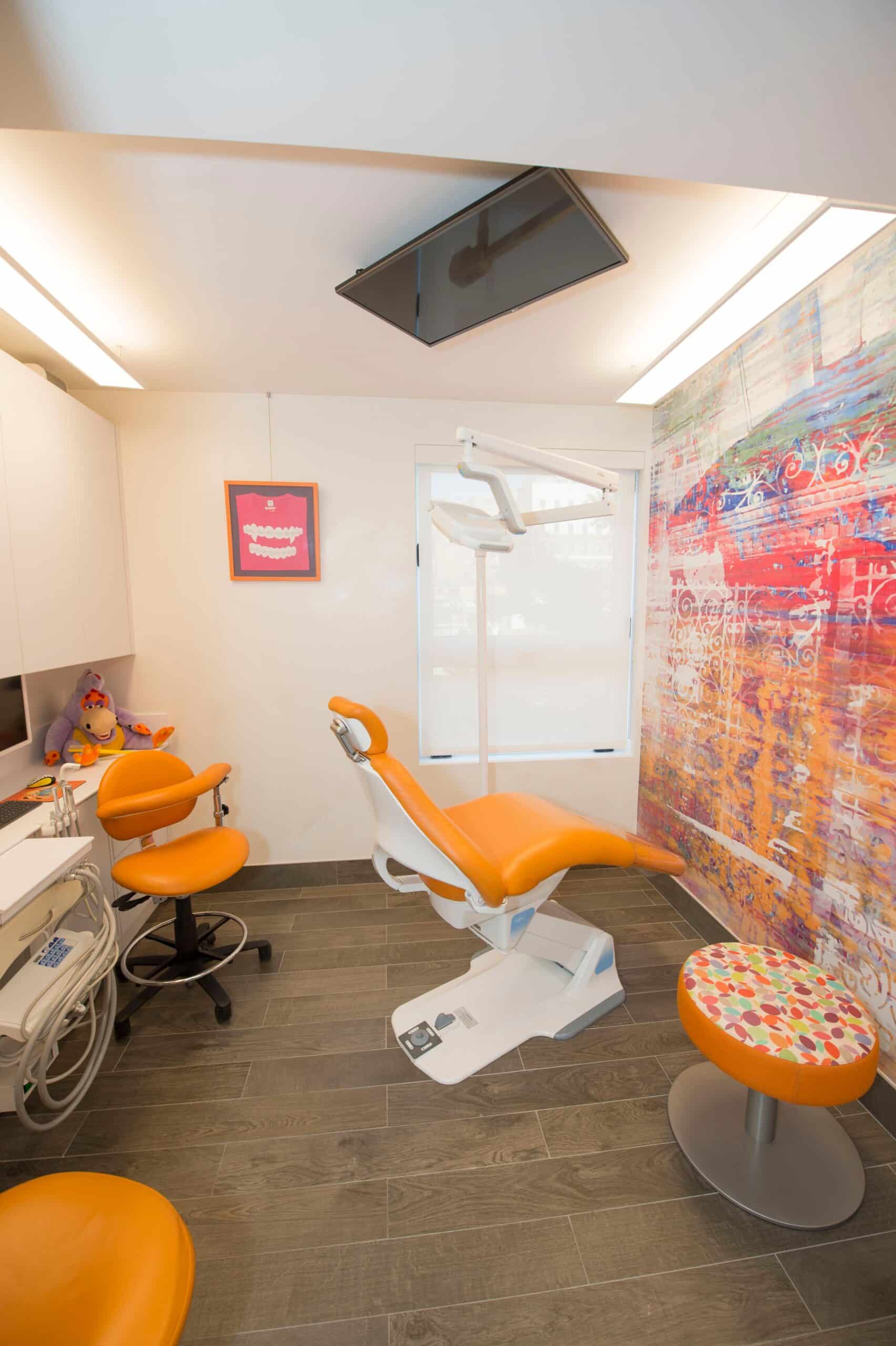 Exam room with an orange dental chair, patterned stool, and abstract mural