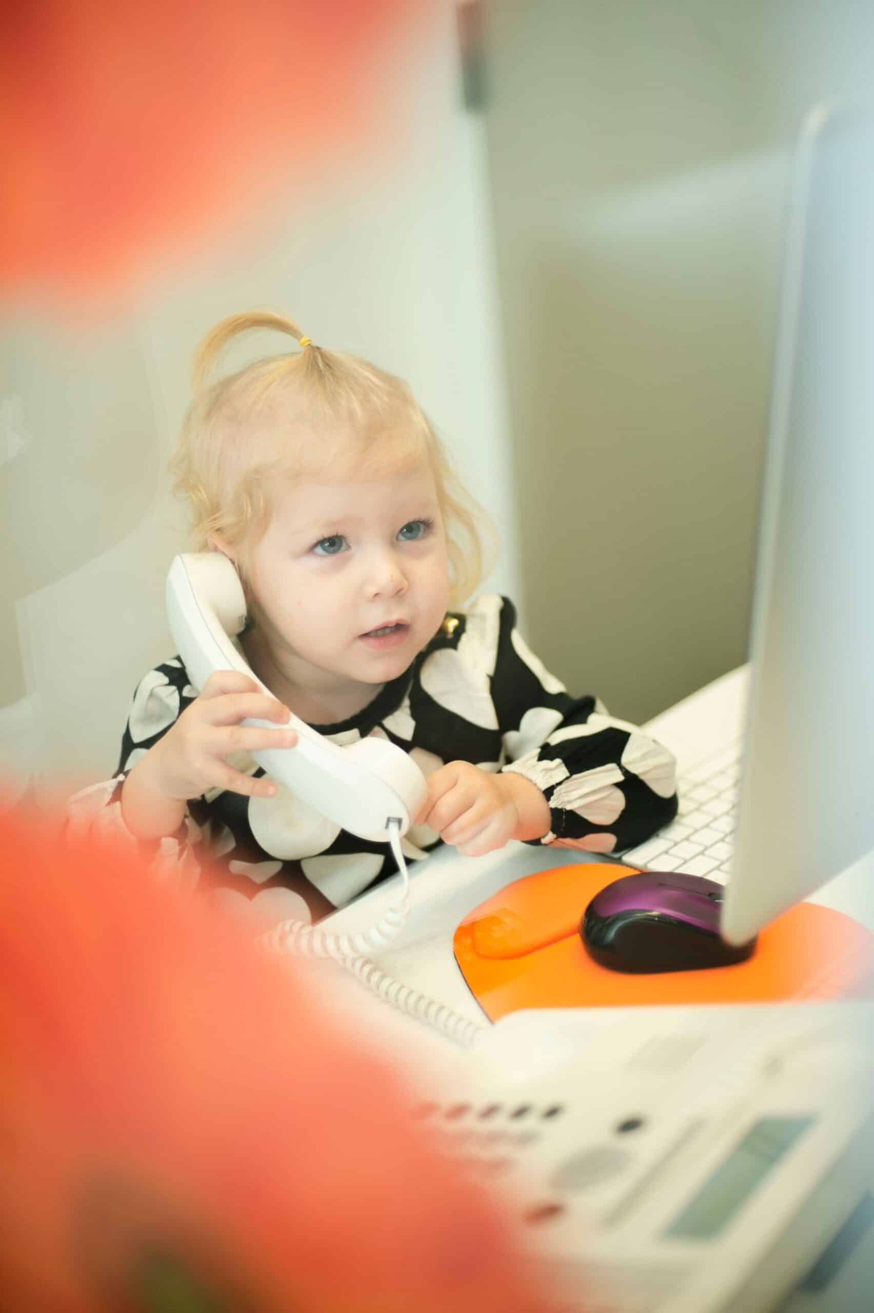 Young child holding a phone handset at the front desk computer