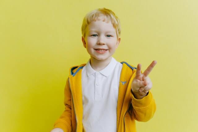 Smiling boy in a yellow jacket giving a peace sign — kids dental care in NYC