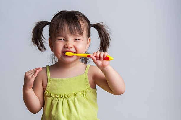 a little kid in avocado green dress with pigtails brushing her teeth