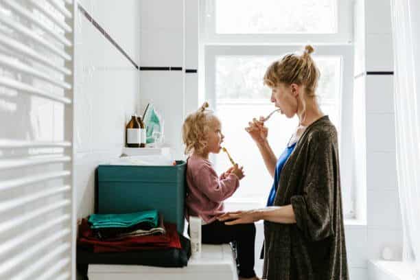 a mother teaching her child how to brush her teeth inside the bathroom