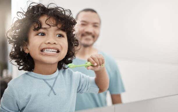 Kid being guided by his dad while brushing his teeth