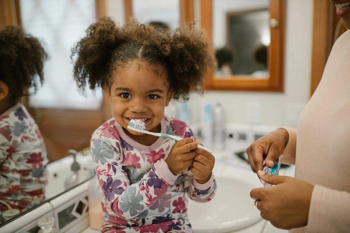 a little kid learning how to brush her teeth while her mother guides her