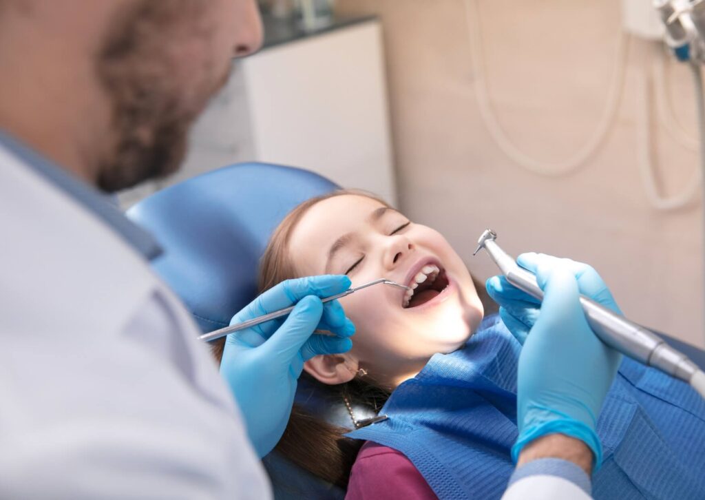Pediatric dentist examining a child's teeth during an appointment to evaluate the need for a dental spacer after early tooth loss.