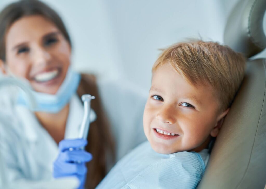 Smiling child seated in a dental chair while a pediatric dentist creates a calm, welcoming environment before a dental exam.